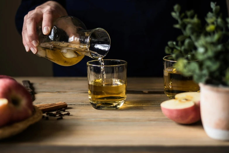 a person pouring apple cid into a glass, a still life, unsplash, square, whisky, seasonal, on a wooden table