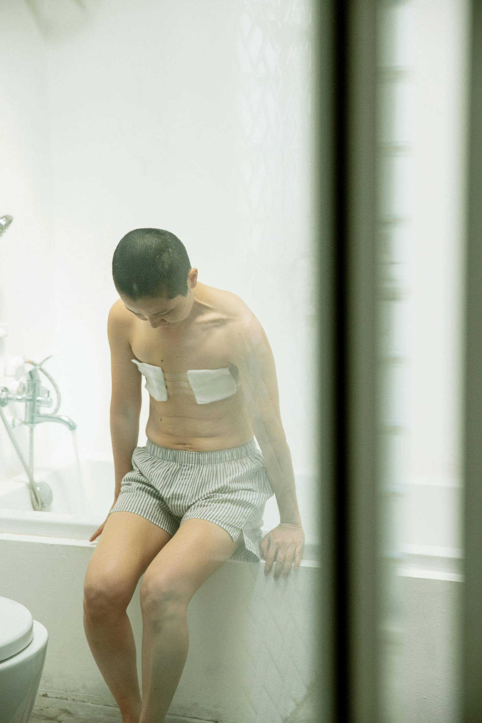 a man sitting on the edge of a bathtub next to a toilet, inspired by Zhang Kechun, happening, battle scars across body, wearing translucent sheet, teenage boy, medical image