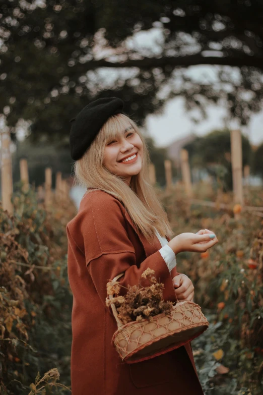 a woman standing in a field holding a basket of flowers, pexels contest winner, brown sweater, smiling :: attractive, lalisa manobal, wearing a beret