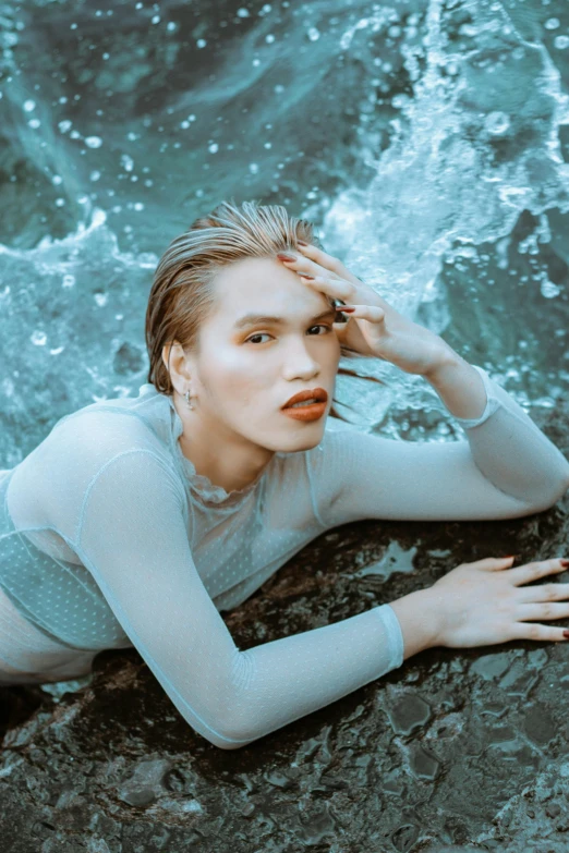 a woman laying on top of a rock next to the ocean, an album cover, inspired by Elsa Bleda, trending on pexels, lipstick, nonbinary model, wet look, blue gray