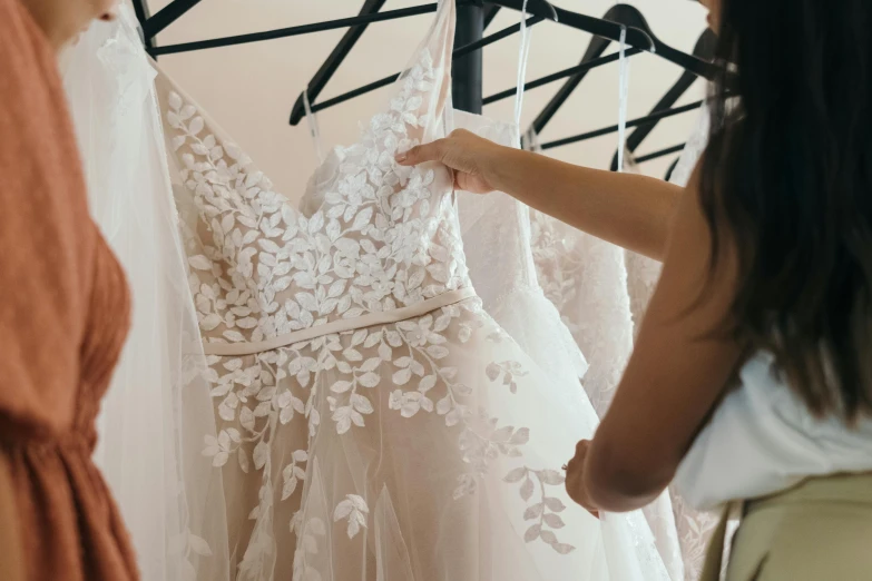 a woman looking at a dress on a hanger, pexels contest winner, wearing ivory colour dress, brittney lee, thumbnail, unedited