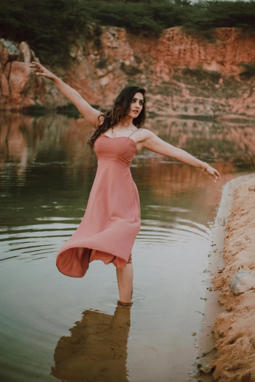 a woman in a pink dress standing in a body of water, pexels contest winner, arabesque, red river, doing a sassy pose, near pond, canyon