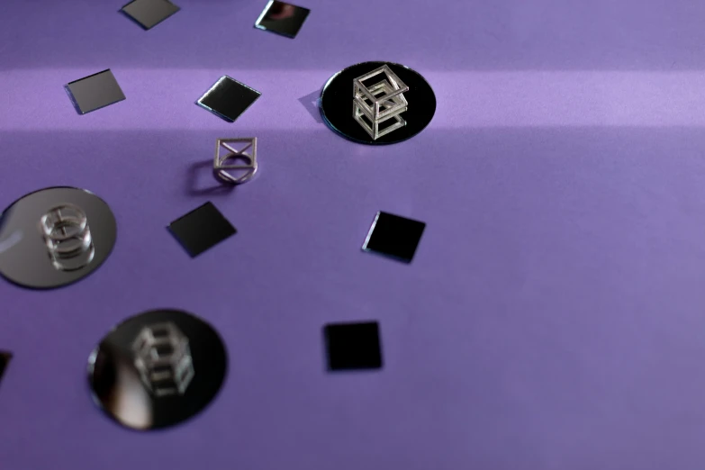 a bunch of magnets sitting on top of a purple surface, a hologram, inspired by Victor Vasarely, trending on pexels, floating symbols, black jewellery, detail shot, square shapes