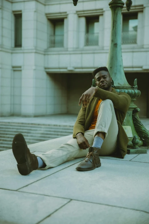 a man sitting on the ground in front of a building, by Stokely Webster, green corduroy pants, in muted colors, jaylen brown, classical