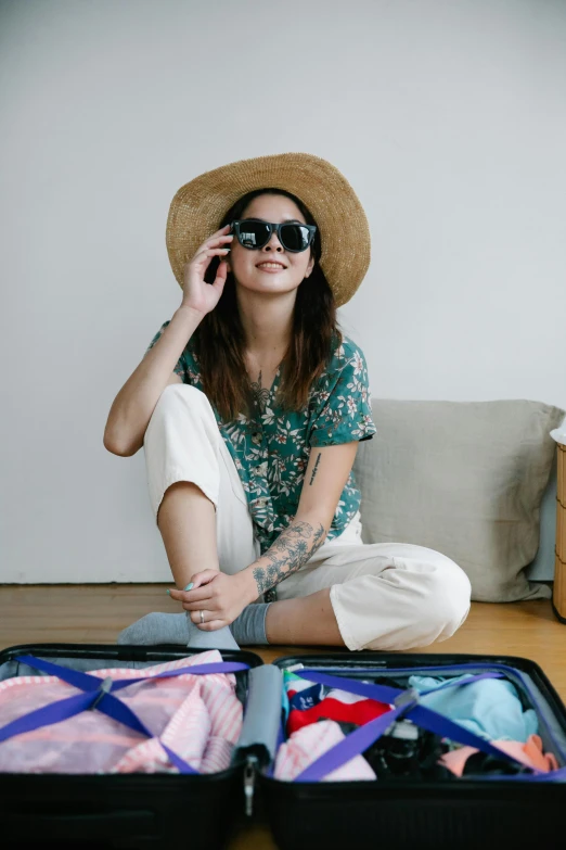 a woman sitting on the floor next to a suitcase, wearing sunglasses and a hat, implanted sunglasses, wearing a linen shirt, connectivity