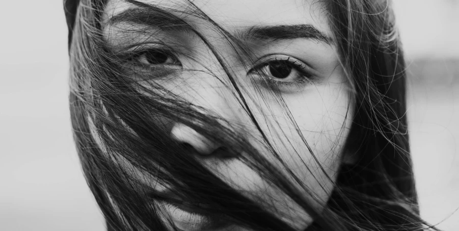 a woman with long hair blowing in the wind, a black and white photo, by irakli nadar, pexels contest winner, realism, slit pupils, asian face, hiding, closeup portrait