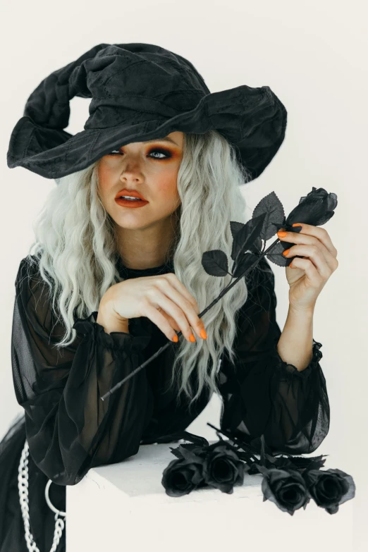 a woman in a witch costume holding a rose, trending on pexels, gothic art, curly white hair, black hat, sydney sweeney, square