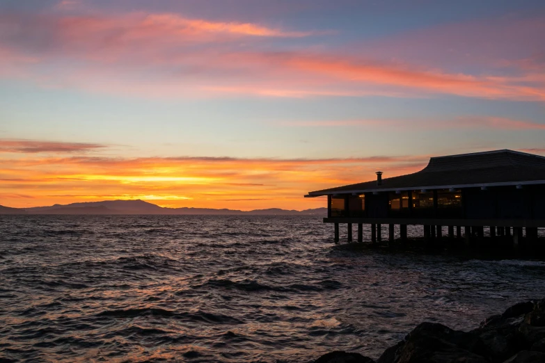 a building sitting on top of a body of water, inspired by Edwin Georgi, pexels contest winner, vibrant sunset, bay, near a jetty, sf