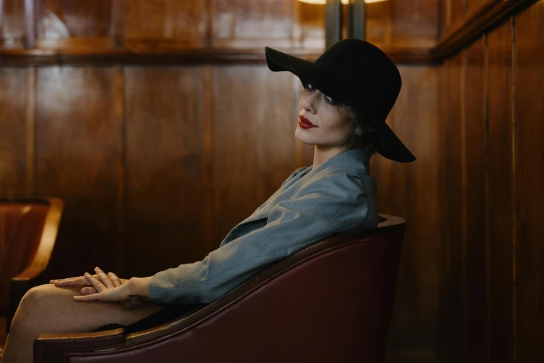 a woman sitting in a chair wearing a hat, by Emma Andijewska, pexels contest winner, gentleman's club lounge, with high cheekbones, tall, lena oxton