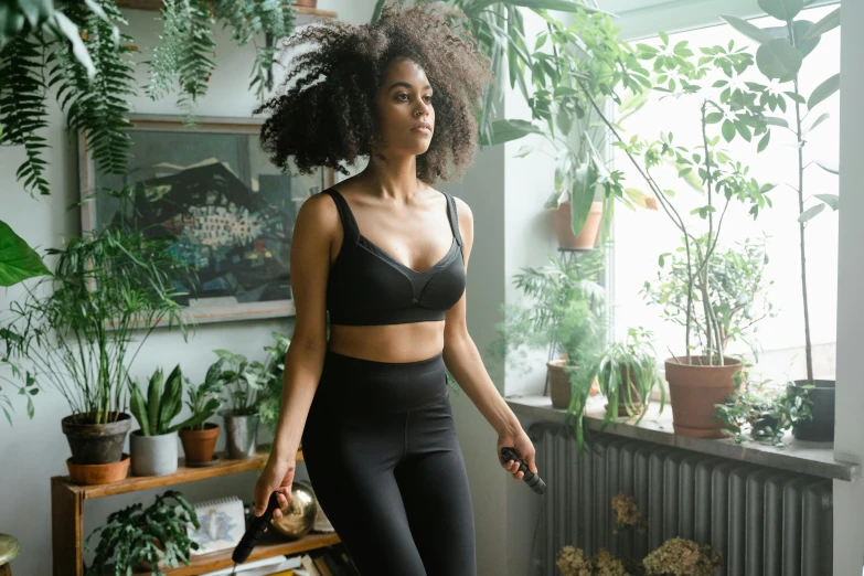 a woman standing in front of a window holding a tennis racquet, inspired by Esaias Boursse, trending on pexels, happening, wearing a cropped black tank top, covered in plants, sexy black woman walks past them, wearing a tracksuit