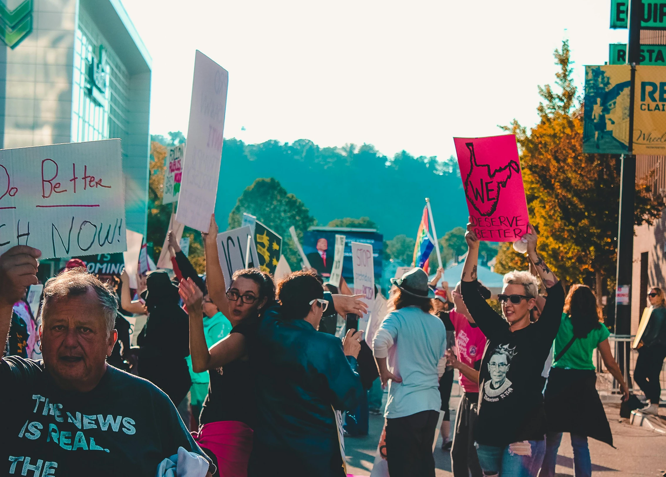 a group of people walking down a street holding signs, a photo, by Lee Loughridge, pexels, arms raised, hills in the background, people with mohawks, background image