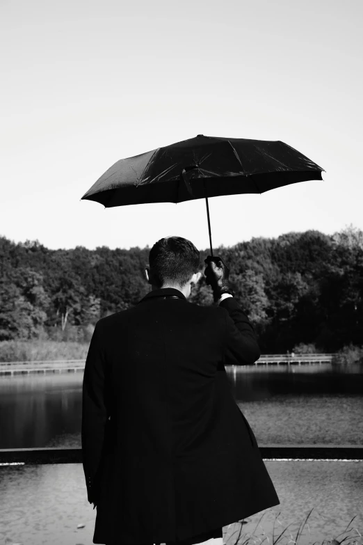 a black and white photo of a man holding an umbrella, unsplash, album cover art, near a lake, profile picture, dark. no text