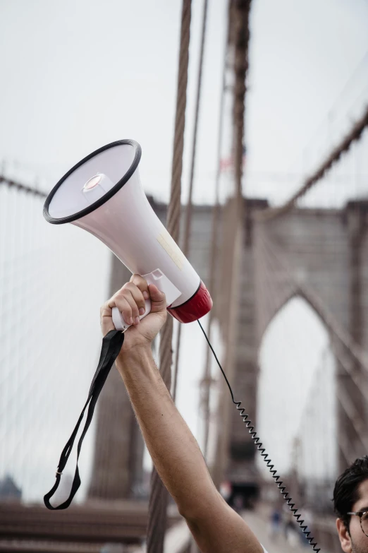 a man holding a megaphone in front of a bridge, unsplash, brooklyn, holding a staff, protest, blank