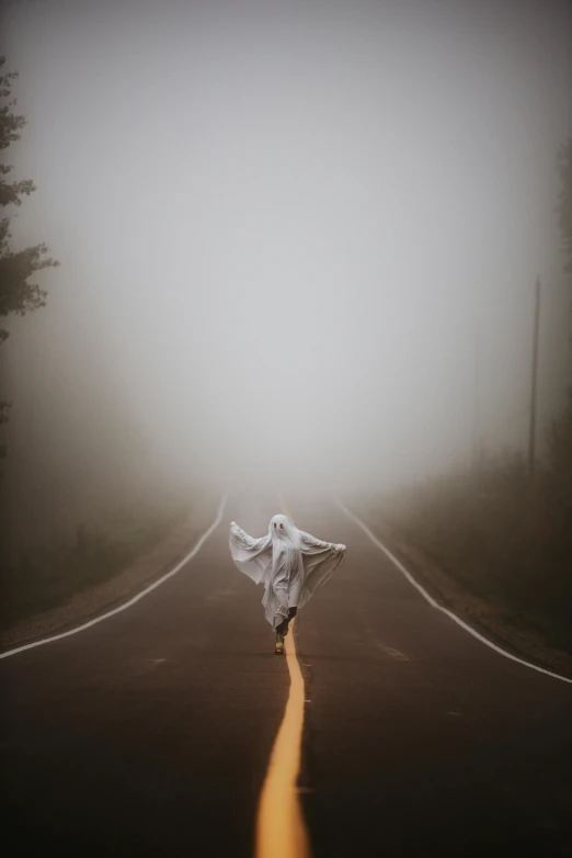 a person walking down a road on a foggy day, inspired by Brooke Shaden, unsplash contest winner, wearing torn white cape, scary pose, photograph ”