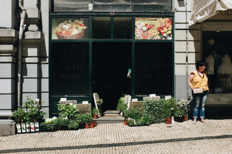 a woman standing in front of a flower shop, a photo, lisbon, building facing, fruit and flowers, ground level