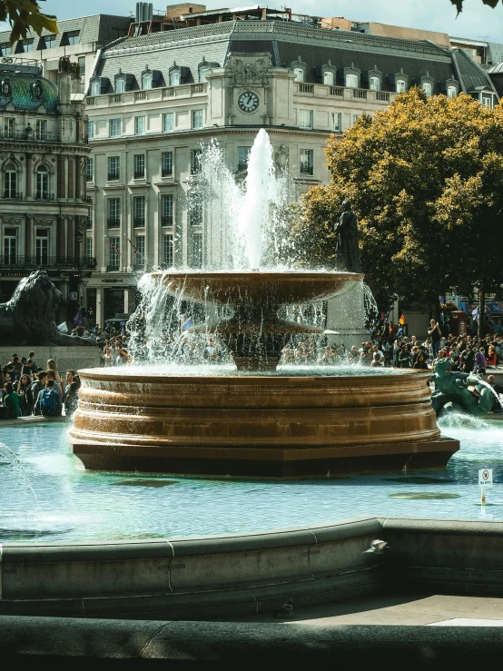 a group of people standing around a fountain, london architecture, during the day, monuments, pools of water
