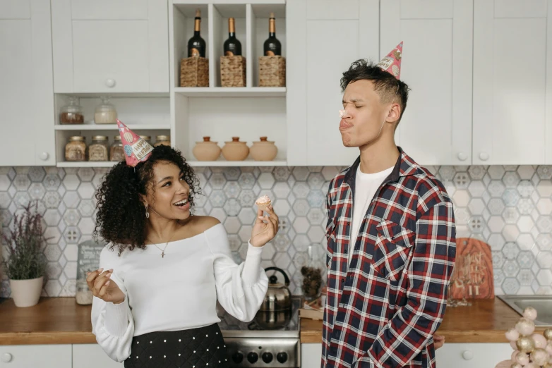 a man standing next to a woman in a kitchen, a photo, pexels, happening, party hats, background image, curls on top, holding a candle holder