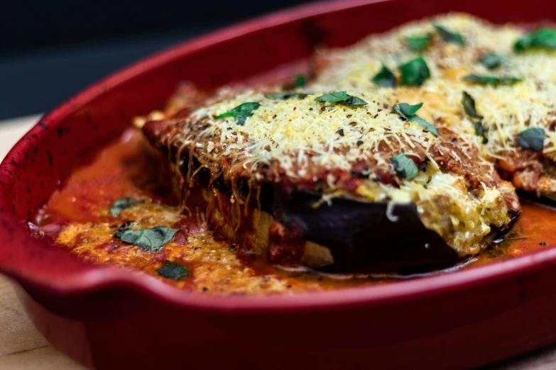 a close up of a dish of food on a table, eggplant, in a red dish, cheesy, stuffed