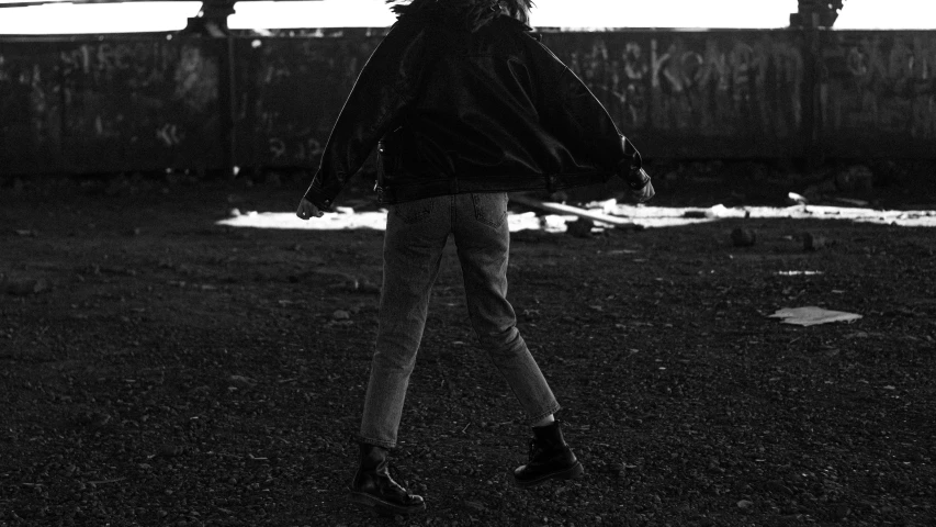 a black and white photo of a woman walking, an album cover, pexels, antipodeans, wearing jeans and a black hoodie, gritty feeling, black jacket | shiny, back and standing