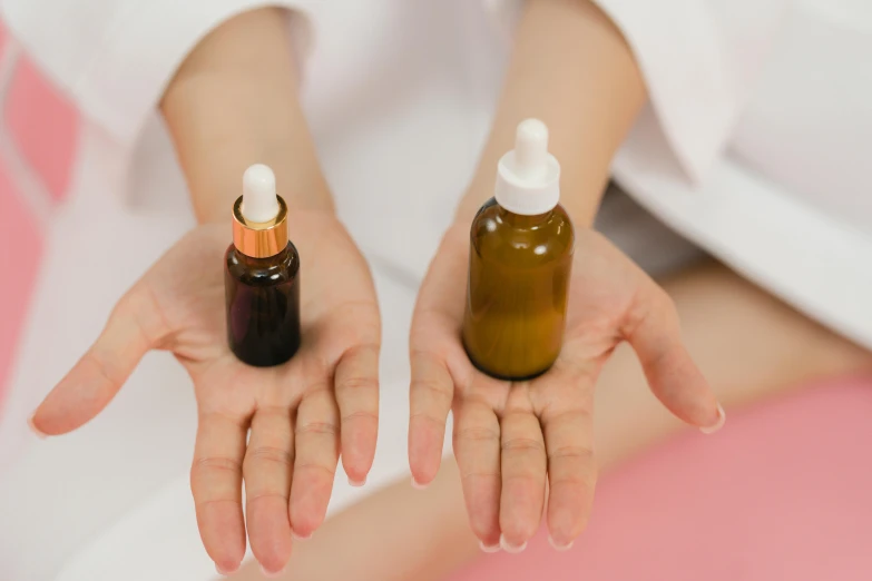 a woman holding two bottles of liquid in her hands, by Olivia Peguero, trending on pexels, renaissance, candy treatments, partially cupping her hands, brown, manuka