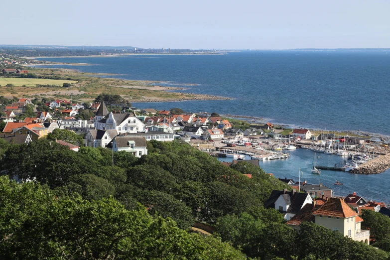 a group of houses sitting on top of a lush green hillside, inspired by Wilhelm Marstrand, pexels, art nouveau, view of sea, oland, white buildings with red roofs, brown