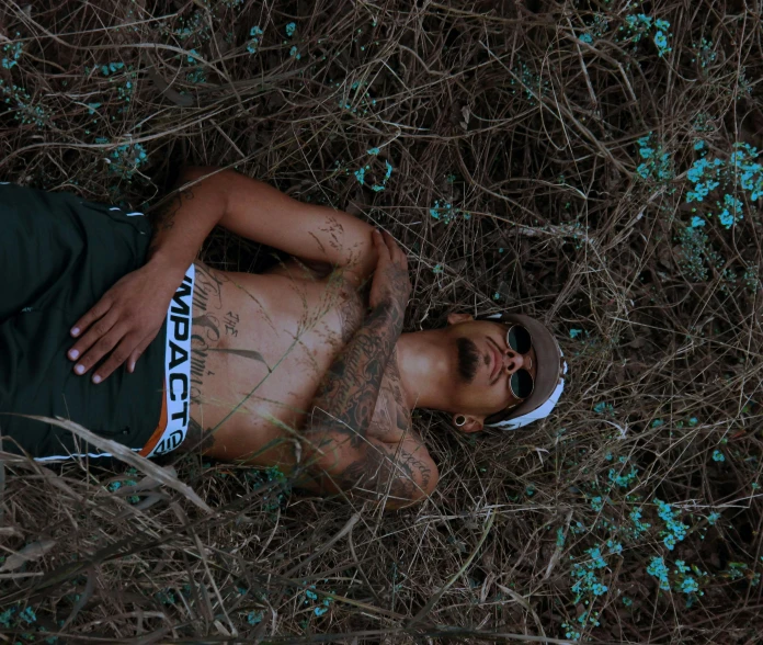a man that is laying down in the grass, by Elsa Bleda, pexels contest winner, graffiti, barechest, bad bunny, trees growing on its body, light skin
