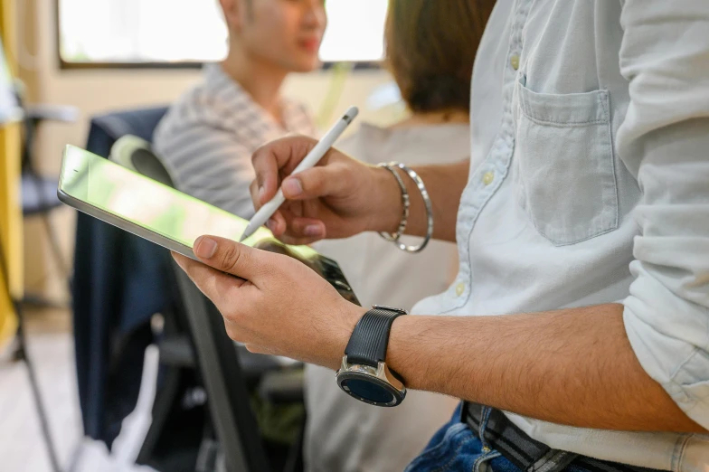 a man holding a pen and writing on a tablet, a cartoon, trending on pexels, standing in class, over the shoulder closeup, took on ipad, sitting with wrists together