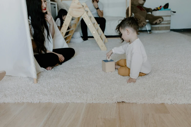 a little boy sitting on the floor playing with a toy, by Emma Andijewska, pexels contest winner, moist brown carpet, a group of people, background image, gif