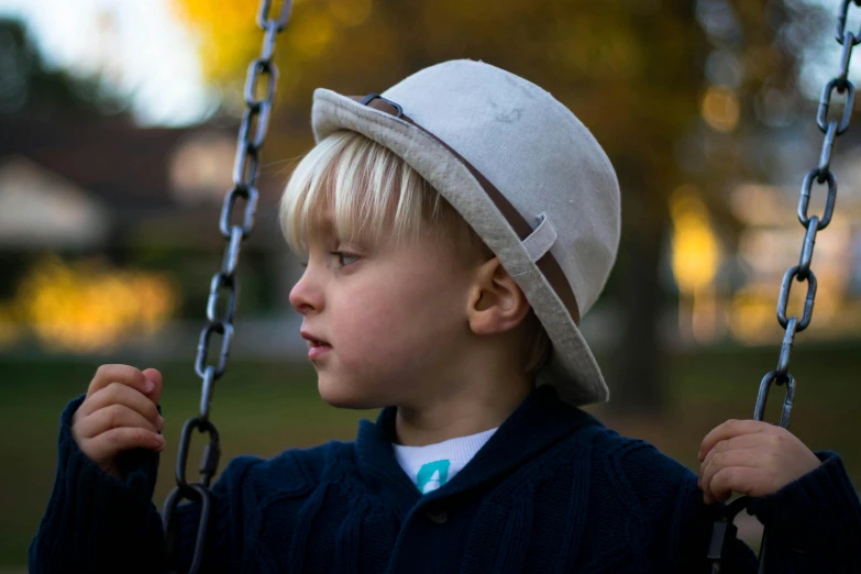 a little boy that is sitting on a swing, inspired by Kate Greenaway, unsplash, white hat, 7 0 mm portrait, close up photograph, grey