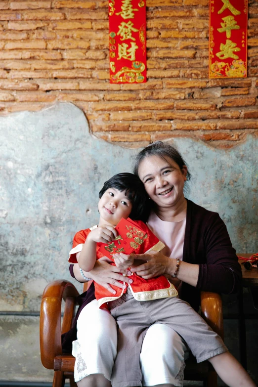 a woman sitting in a chair holding a child, inspired by Cui Bai, happening, while smiling for a photograph, 5 years old, a quaint, square