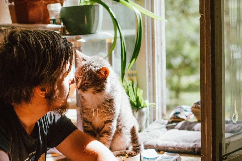 a man sitting at a table with a cat, pexels contest winner, window sill with plants, kissing together cutely, profile image, cottagecore hippie