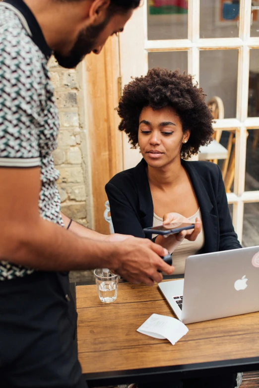 a couple of people sitting at a table with a laptop, trending on unsplash, african american woman, at checkout, square, goddess checking her phone