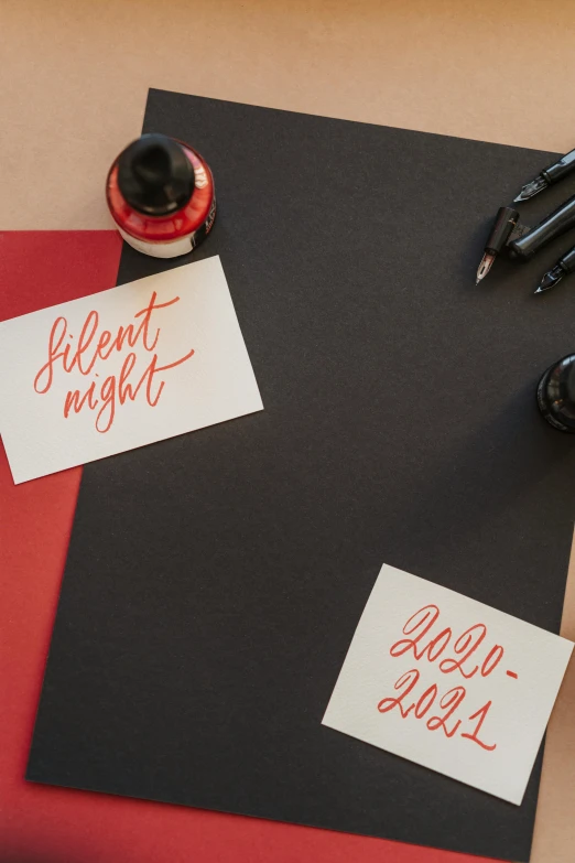 a close up of a piece of paper with writing on it, by Julia Pishtar, unsplash contest winner, letterism, black-crimson color scheme, christmas night, pair of keycards on table, “modern calligraphy art