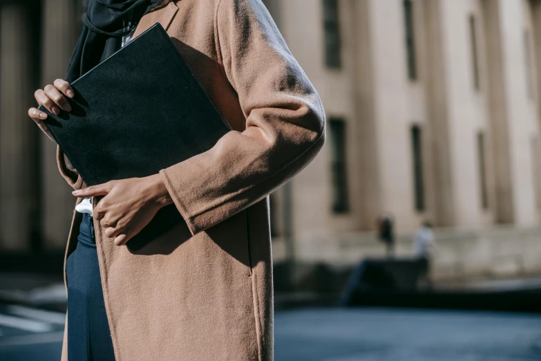 a man in a coat and scarf holding a laptop, trending on pexels, woman in black robes, academic clothing, light brown coat, ameera al-taweel