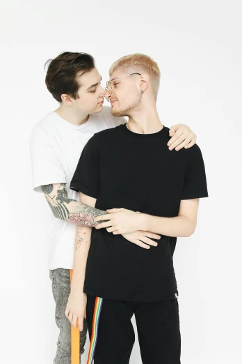 a couple of men standing next to each other, non binary model, wearing a black t-shirt, kissing each other, official store photo