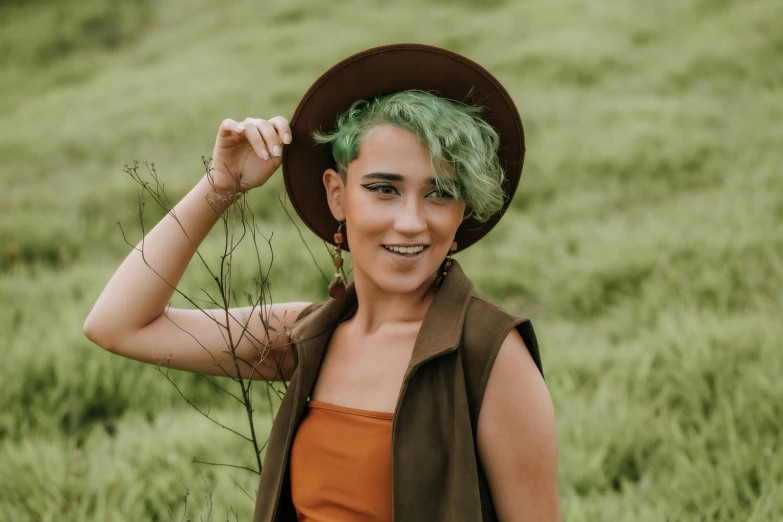 a woman with green hair standing in a field, trending on pexels, caracter with brown hat, avatar image, non binary model, smiling young woman