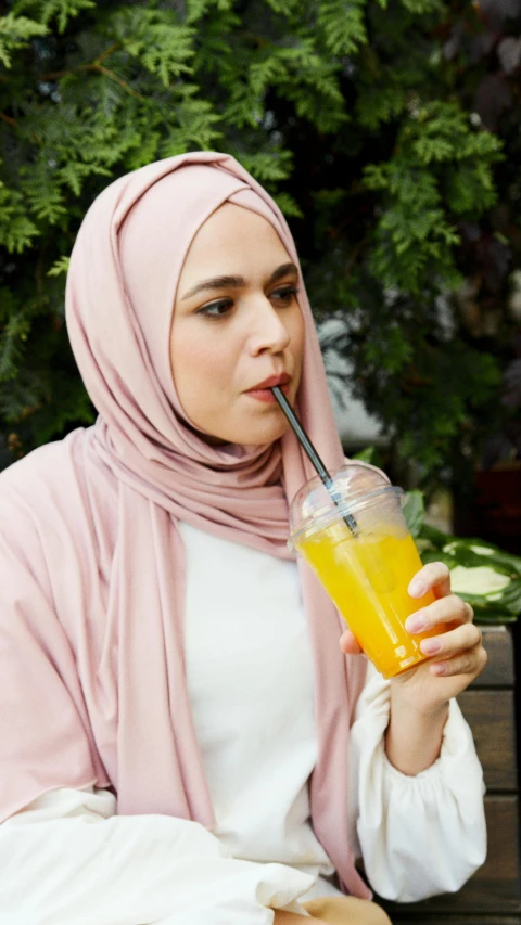 a woman sitting on a bench drinking a drink, a cartoon, pexels, hurufiyya, hijab, wearing wheat yellow gauze, stainless steel, press photos