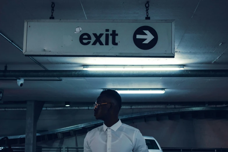 a man standing in a parking garage next to a exit sign, an album cover, pexels contest winner, excessivism, black man, black. airports, exiting from a wardrobe, ignant