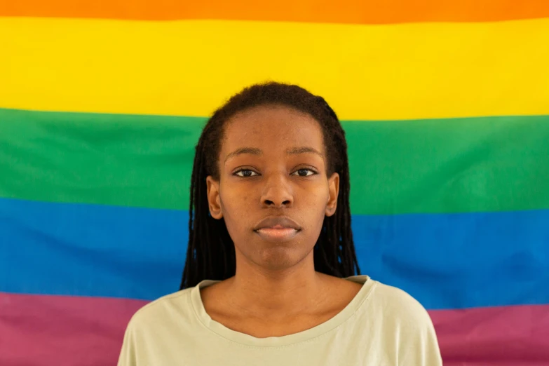 a woman standing in front of a rainbow flag, by Lily Delissa Joseph, black teenage boy, close up portrait photo, on a pale background, portrait featured on unsplash