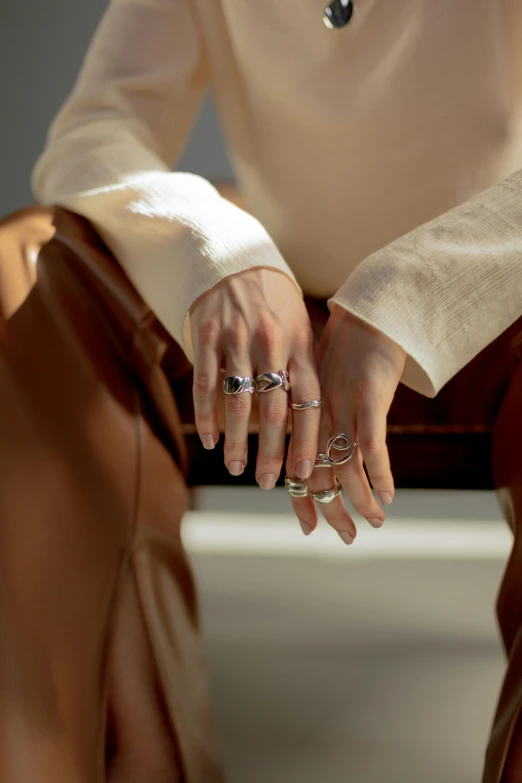 a woman in a white shirt and brown leather pants, a picture, inspired by L. A. Ring, photo of a hand jewellery model, silver，ivory, collection product, detail shot