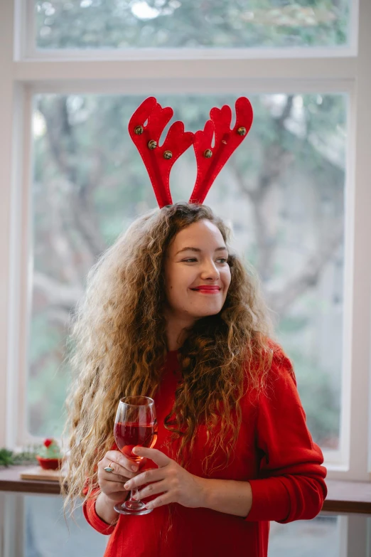 a woman wearing reindeer antlers holding a glass of wine, wavy hair spread out, red, 2019 trending photo, teenager