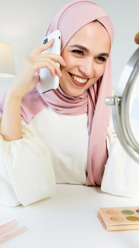 a woman sitting at a table talking on a cell phone, by Basuki Abdullah, trending on pexels, hurufiyya, white and pink, a still of a happy, emir, silver