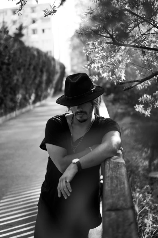 a black and white photo of a man leaning against a fence, a black and white photo, by Giuseppe Avanzi, portrait of johnny depp, wears a destroyed hat, paru itagaki, - n 9