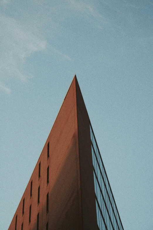 a tall building sitting in front of a blue sky, a picture, pexels contest winner, minimalism, triangular face, black and terracotta, shot from the side, dynamic angled shot