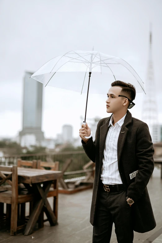 a man standing on top of a roof holding an umbrella, by Basuki Abdullah, unsplash, visual art, wearing a suit and glasses, young man, wearing jacket, in style of lam manh