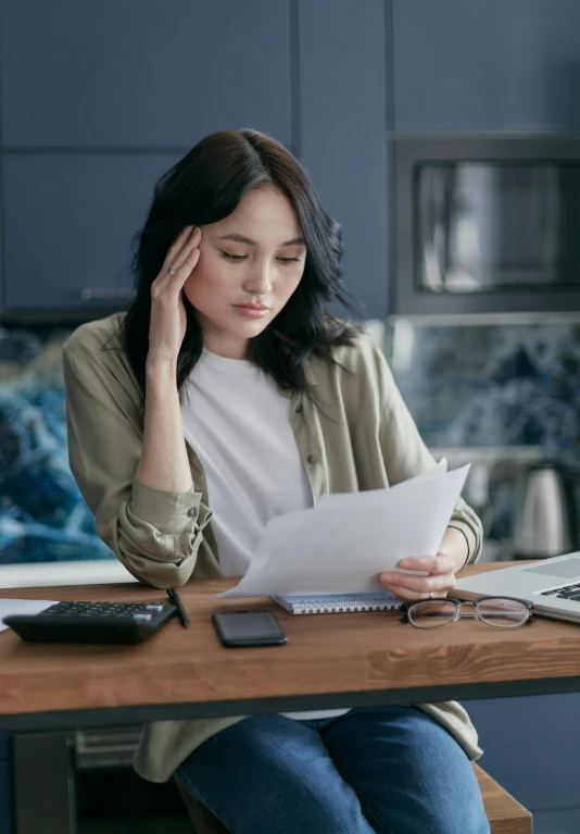 a woman sitting at a table with a laptop and papers, trending on pexels, renaissance, disappointed, selling insurance, an asian woman, woman with braided brown hair