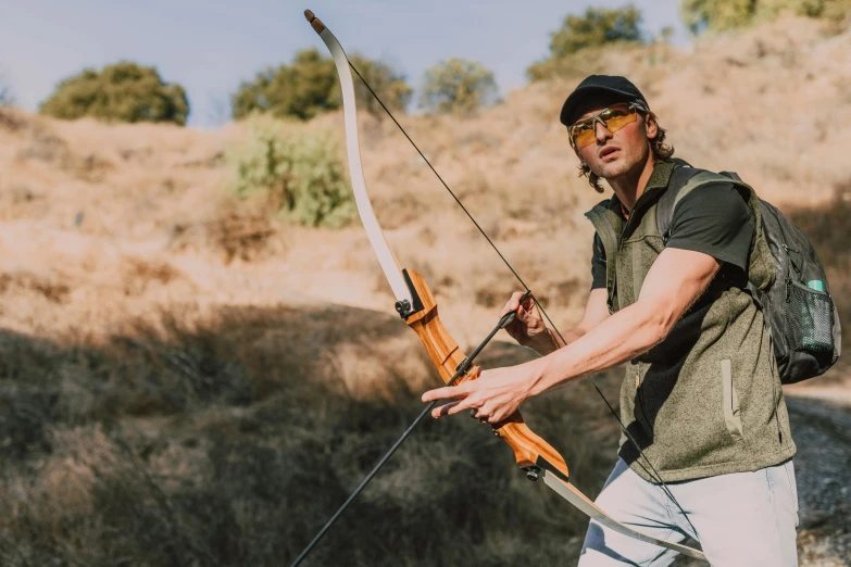 a man with a backpack holding a bow and arrow, a portrait, unsplash, california;, working out in the field, 🦩🪐🐞👩🏻🦳, game ready