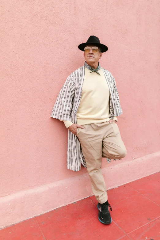 a man leaning against a pink wall wearing a hat, by Pamela Drew, wearing a duster coat, stripey pants, ignacio fernández ríos, white background