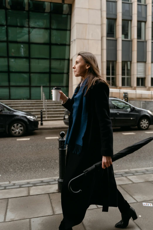 a woman walking down the street with an umbrella, drinking a cup of coffee, wearing black coat, vehicle, portrait featured on unsplash