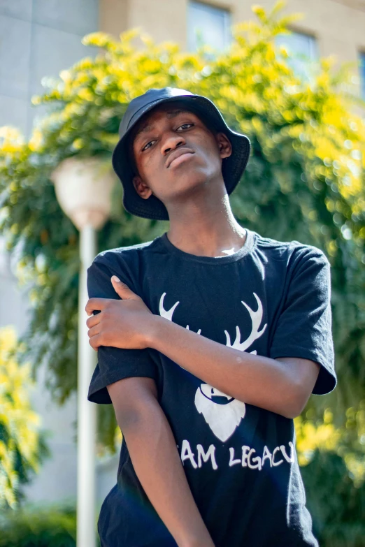 a young man standing in front of a building, iamag premiere, baggy clothing and hat, ( ( dark skin ) ), sitting on a leaf